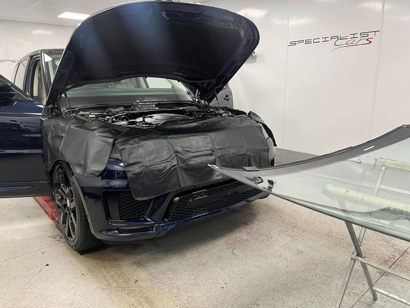 A Range Rover with protective covers over the wings and bonnet and the replacement windscreen waiting on a stand alongside