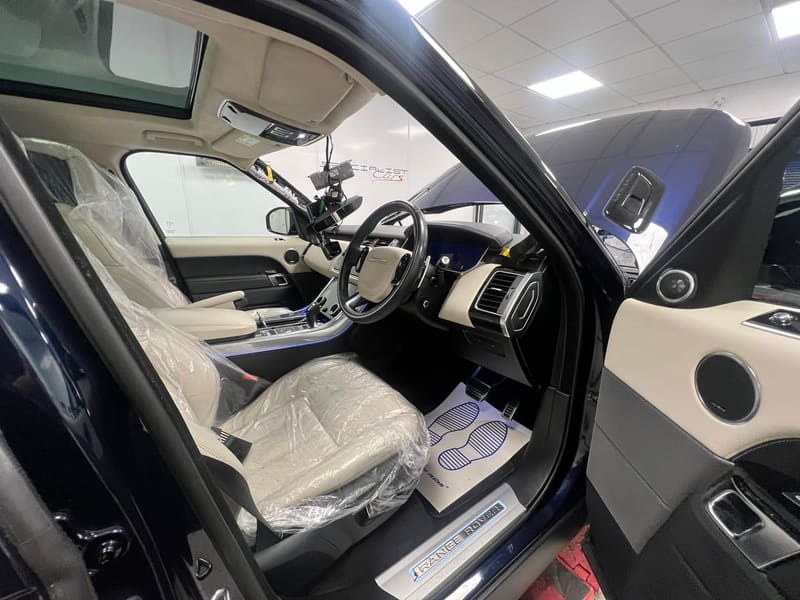 Inside a Range Rover during a windscreen fitting, seats wrapped and floor matted while the glass is set into the aperture