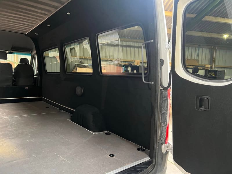 The inside of a lined Mercedes Sprinter looking along a row of three side windows fitted into what were solid panels