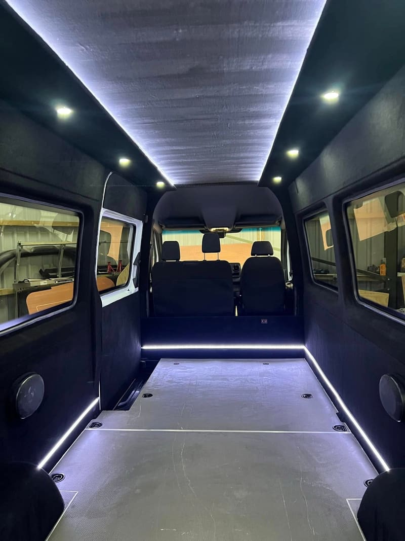 The lined interior of a Sprinter conversion with side windows fitted on both sides and the lighting switched on