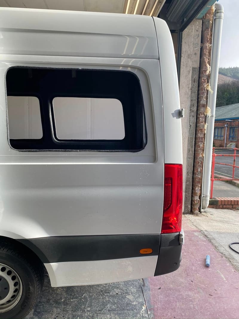 The side panel of a silver Sprinter cut open into a finished aperture, edges sealed, ready for the window to go in